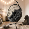 [Black] Black wicker hanging egg chair with black cushions in bedroom with string lights and teddy bear