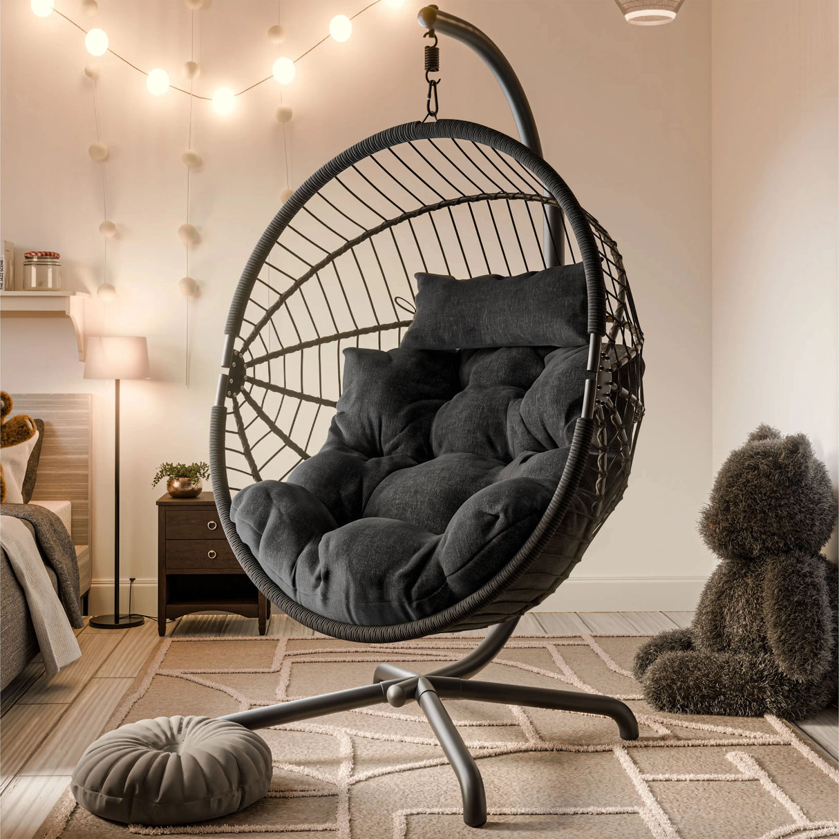 [Black] Black wicker hanging egg chair with black cushions in bedroom with string lights and teddy bear