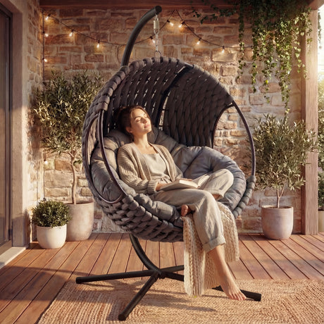Round Hanging Egg Chair - Indoor Outdoor Swinging Egg Chair with stand and cushion, placed on a wooden patio with cozy lighting and potted plants.