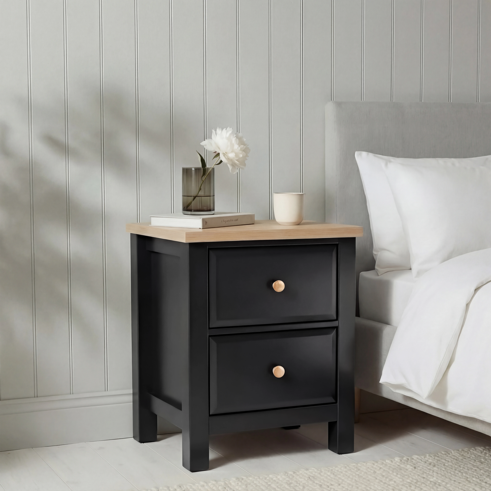 [Black] Haven 2-drawer bedside table in a bedroom lifestyle setting with soft furnishings and lamp in background