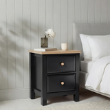 [Black] Haven 2-drawer bedside table in a bedroom lifestyle setting with soft furnishings and lamp in background