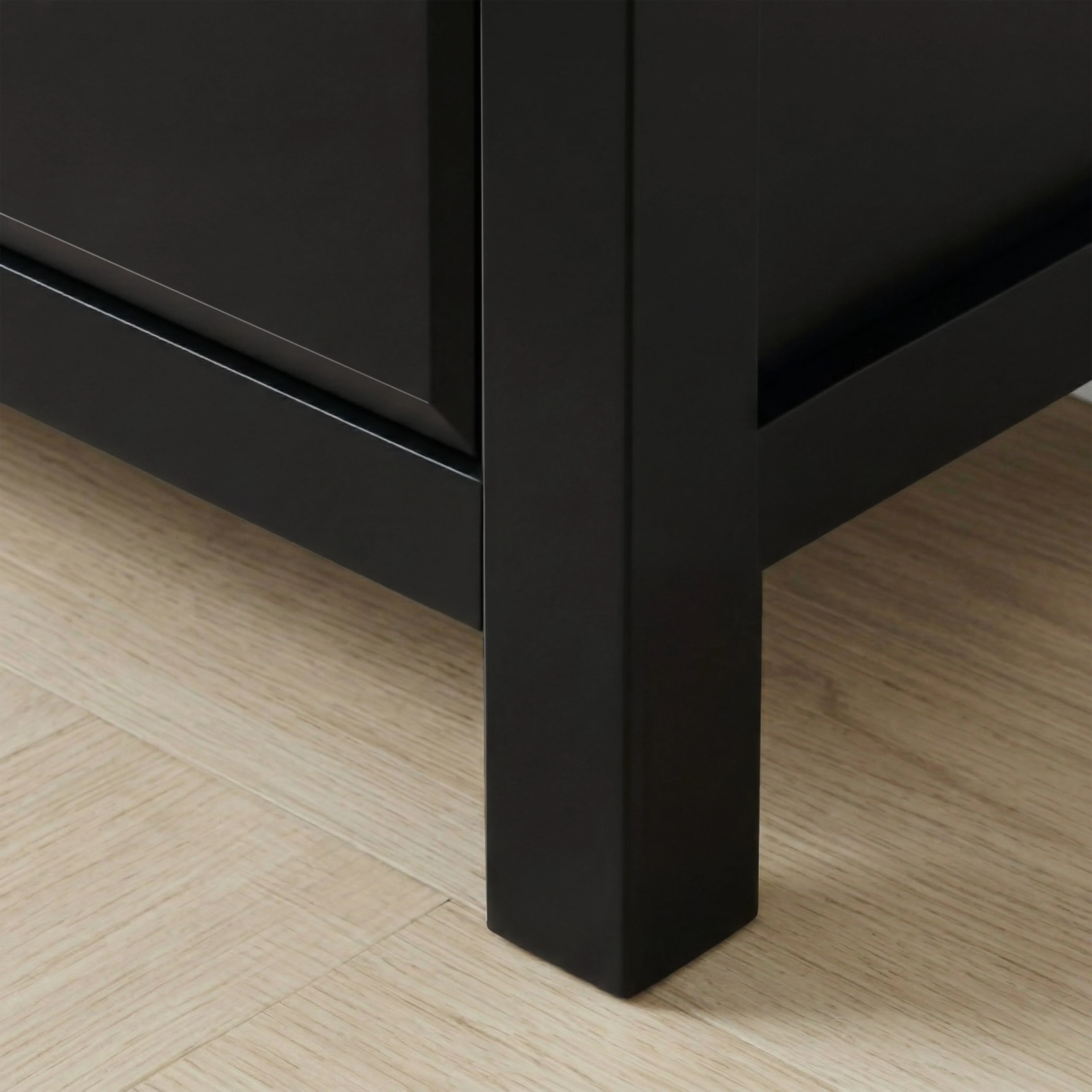 [Black] Haven 5-drawer tall chest angled close-up showing painted frame leg and base detail against wooden floor