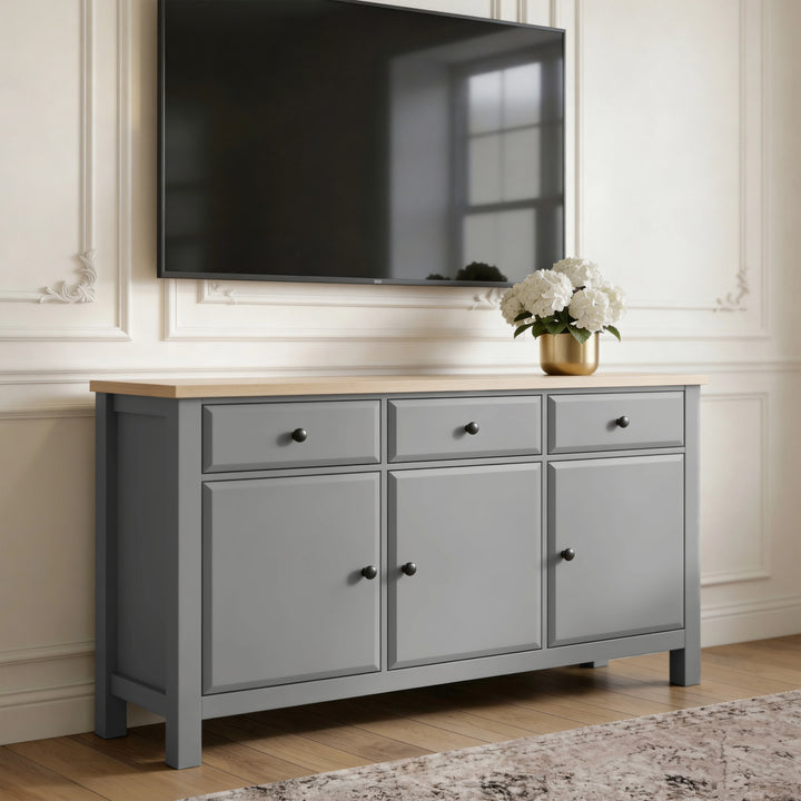 [Grey] Haven 3-door sideboard used as TV stand with wall-mounted flat-screen TV above and gold vase of hydrangeas on oak top