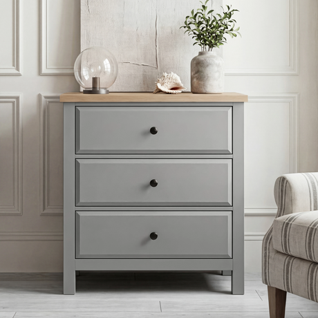 [Grey] Haven 3-drawer chest front view in a neutral styled room with decorative objects on oak veneer top