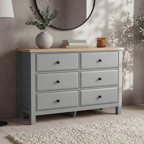 [Grey] Haven 6-drawer chest in a bedroom setting with round mirror, plant and candle on the oak top surface