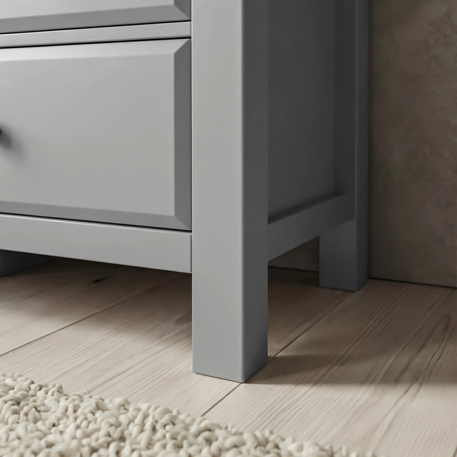 [Grey] Haven chest leg and floor clearance close-up on wide wood planks beside fringed cream rug edge