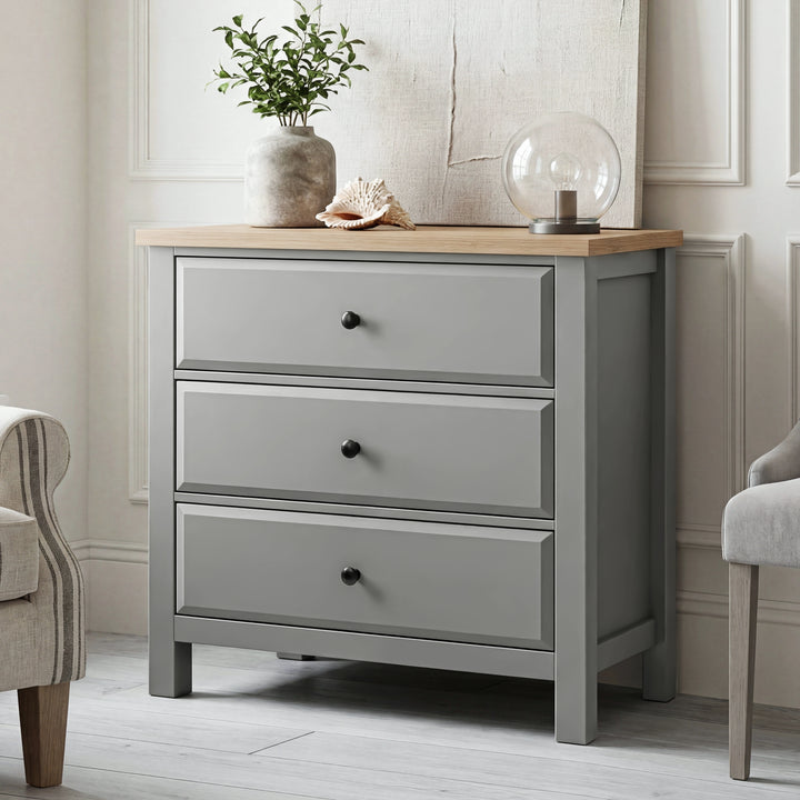 [Grey] Haven 3-drawer chest at angled three-quarter view with ribbed glass orb lamp and stoneware vase on oak top