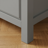 [Grey] Haven 5-drawer tall chest angled close-up showing painted frame leg and base detail against wooden floor