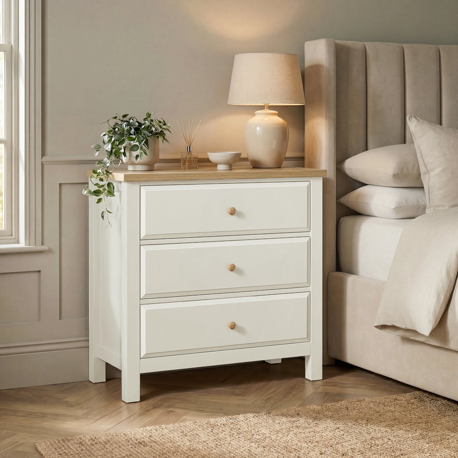 [White] Haven 3-drawer chest in a bedroom setting with lamp on oak top and upholstered headboard panel behind