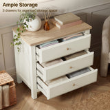 [White] dresser with three drawers on a wooden floor, featuring decorative items on top