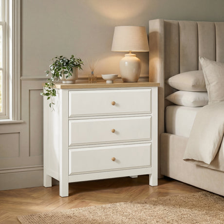 [White] Haven 3-drawer chest in a bedroom setting with lamp on oak top and upholstered headboard panel behind