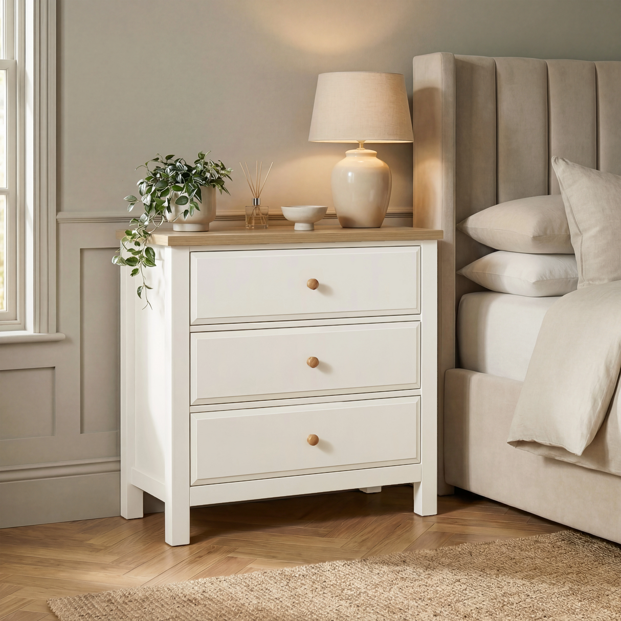 [White] Haven 3-drawer chest in a bedroom setting with lamp on oak top and upholstered headboard panel behind