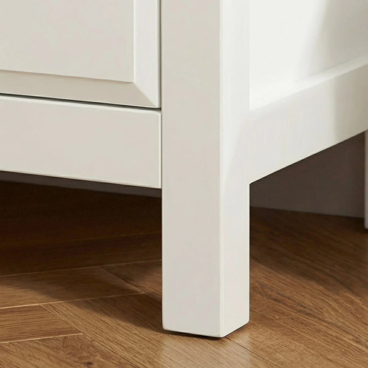 [White] Haven 3-drawer chest angled close-up showing painted frame leg detail and base against a wooden floor