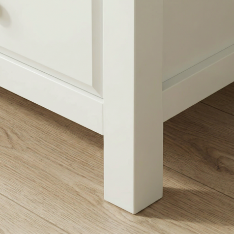 [White] Haven 5-drawer tall chest angled close-up showing painted frame leg and base detail against wooden floor