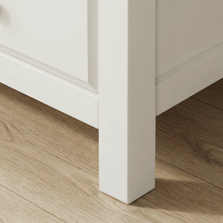[White] Haven 5-drawer tall chest angled close-up showing painted frame leg and base detail against wooden floor