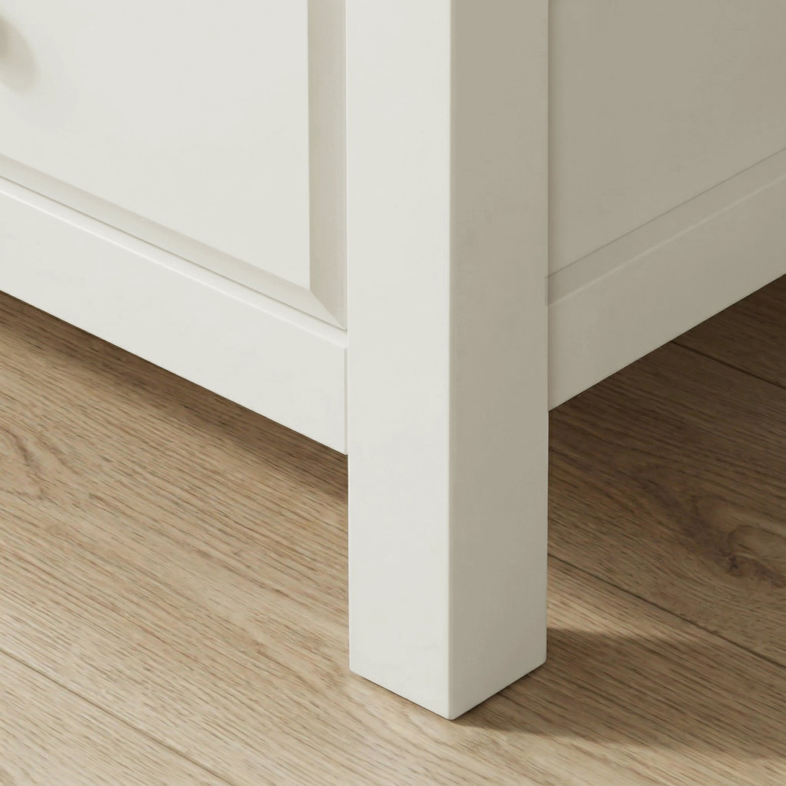 [White] Haven 5-drawer tall chest angled close-up showing painted frame leg and base detail against wooden floor