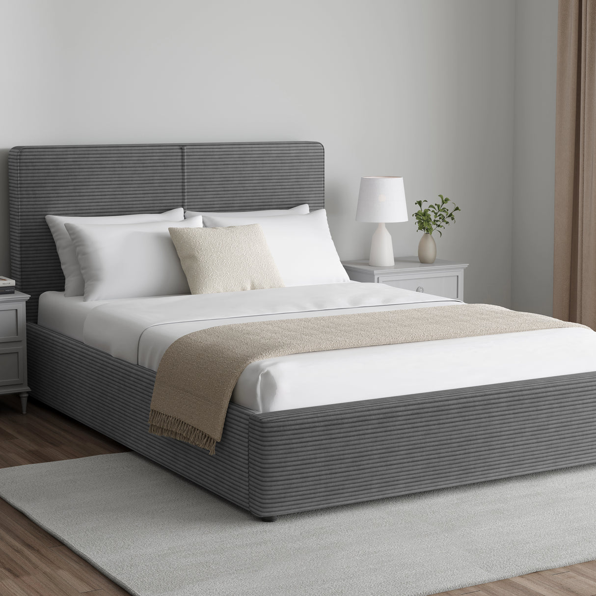 Corduroy ribbed velvet upholstered ottoman bed frame with storage in dark grey, shown in a modern bedroom with white bedding and side tables.