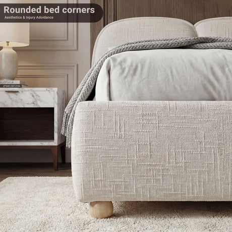 Close view of a beige fabric-wrapped bed base end with rounded edges, textured upholstery, and a low-profile stance on the floor