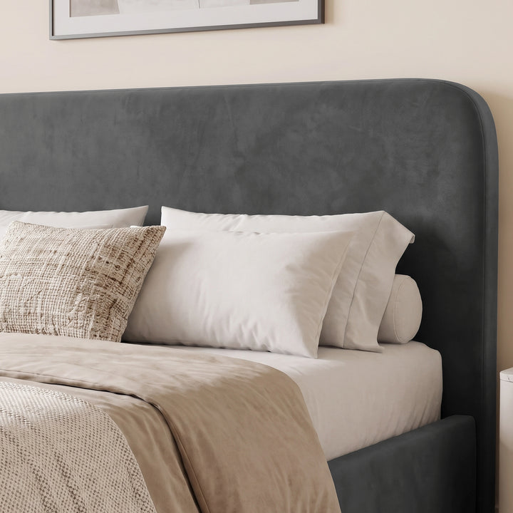 [King | Grey] A dark gray upholstered bed frame with a tall rounded headboard, styled with white pillows and beige bedding in a softly lit bedroom.