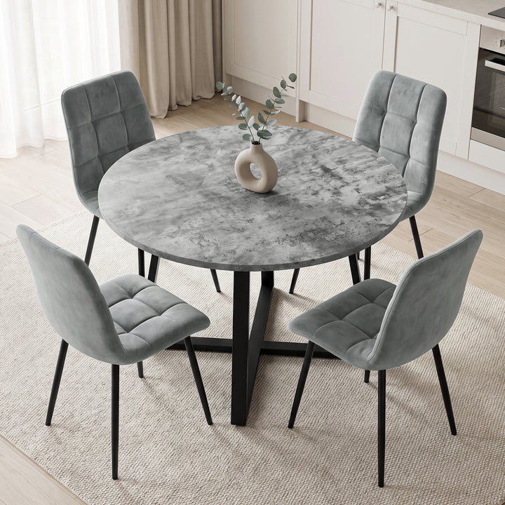 [Light Grey] A round gray marble-patterned dining table with a black metal pedestal base, surrounded by four gray tufted velvet chairs with black legs, set in a bright, modern dining room.