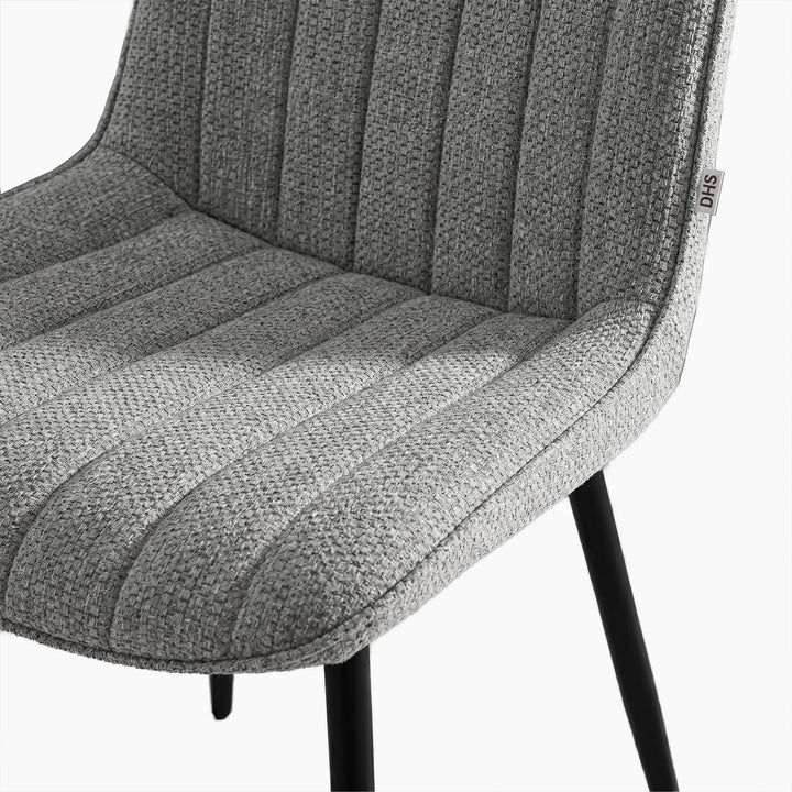 [Vertical Grey | Clear] Close-up of Kyvon grey upholstered fabric channeled stitched chair seat with black metal legs