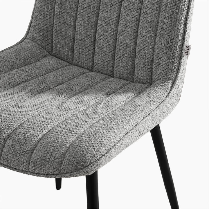 [Vertical Grey | Clear] Close-up of Kyvon grey upholstered fabric channeled stitched chair seat with black metal legs