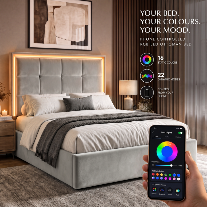 [Light Grey | Double] bedroom scene shows a light grey upholstered bed with a glowing LED headboard and a hand holding a smartphone that displays the app controlling the bed lights.