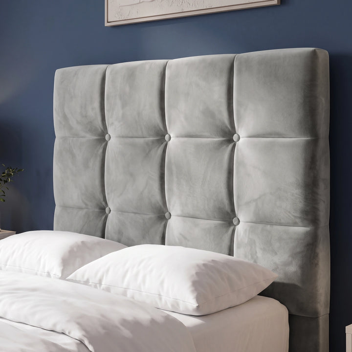 [Single | Grey] square upholstered headboard in a light gray velvet fabric with a tufted grid pattern and decorative buttons, shown on a bed with white bedding against a dark blue wall.