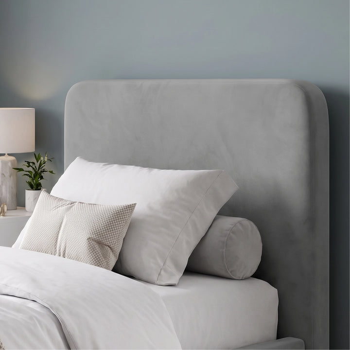 [Light Grey | Small Double] A modern upholstered bed headboard in a soft grey velvet fabric, styled with white bedding, two white pillows, and a cylindrical gray pillow against a muted blue-gray wall.