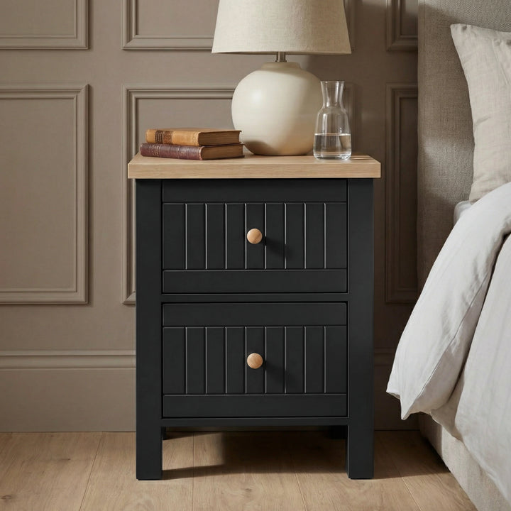 [Black] Linra 2-drawer bedside table front view in a styled bedroom setting with decorative accessories on top