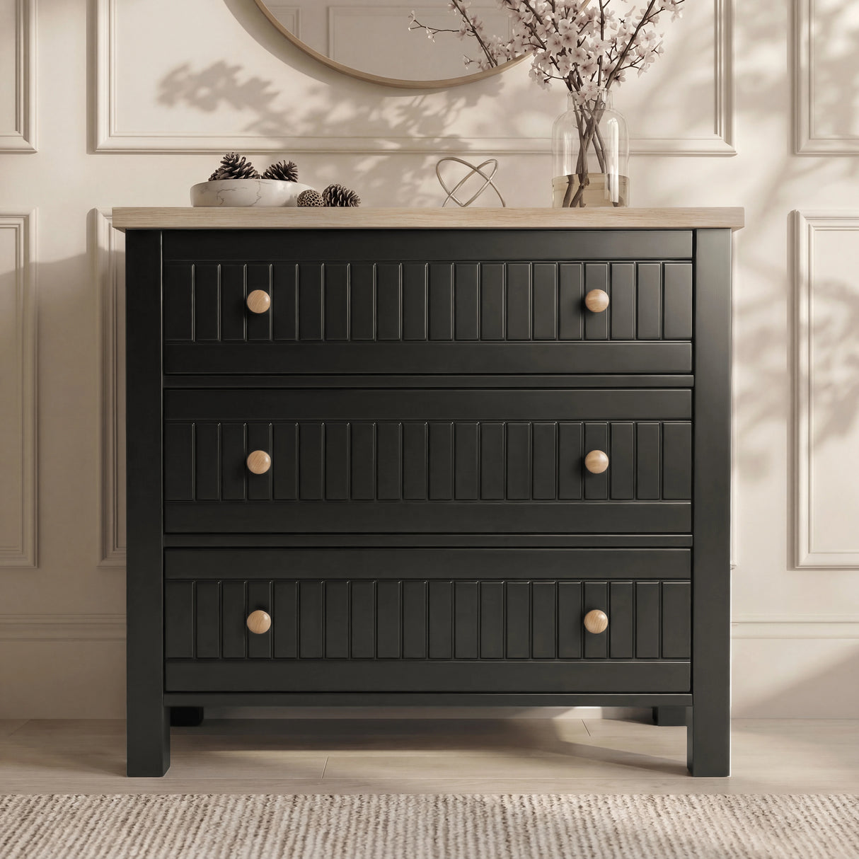 [Black] Linra chest of drawers in black with round mirror above, oak top holding vase of dried branches