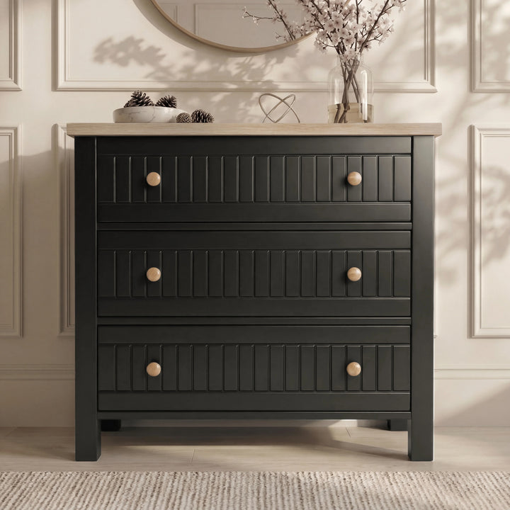 [Black] Linra chest of drawers in black with round mirror above, oak top holding vase of dried branches