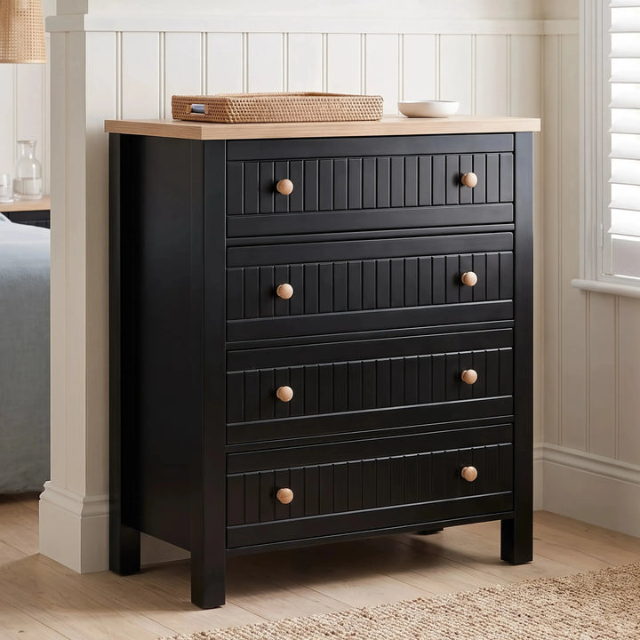 [Black] Linra 4-drawer chest with oak veneer top main front view with basket, rug placed against a beaded cream wall.