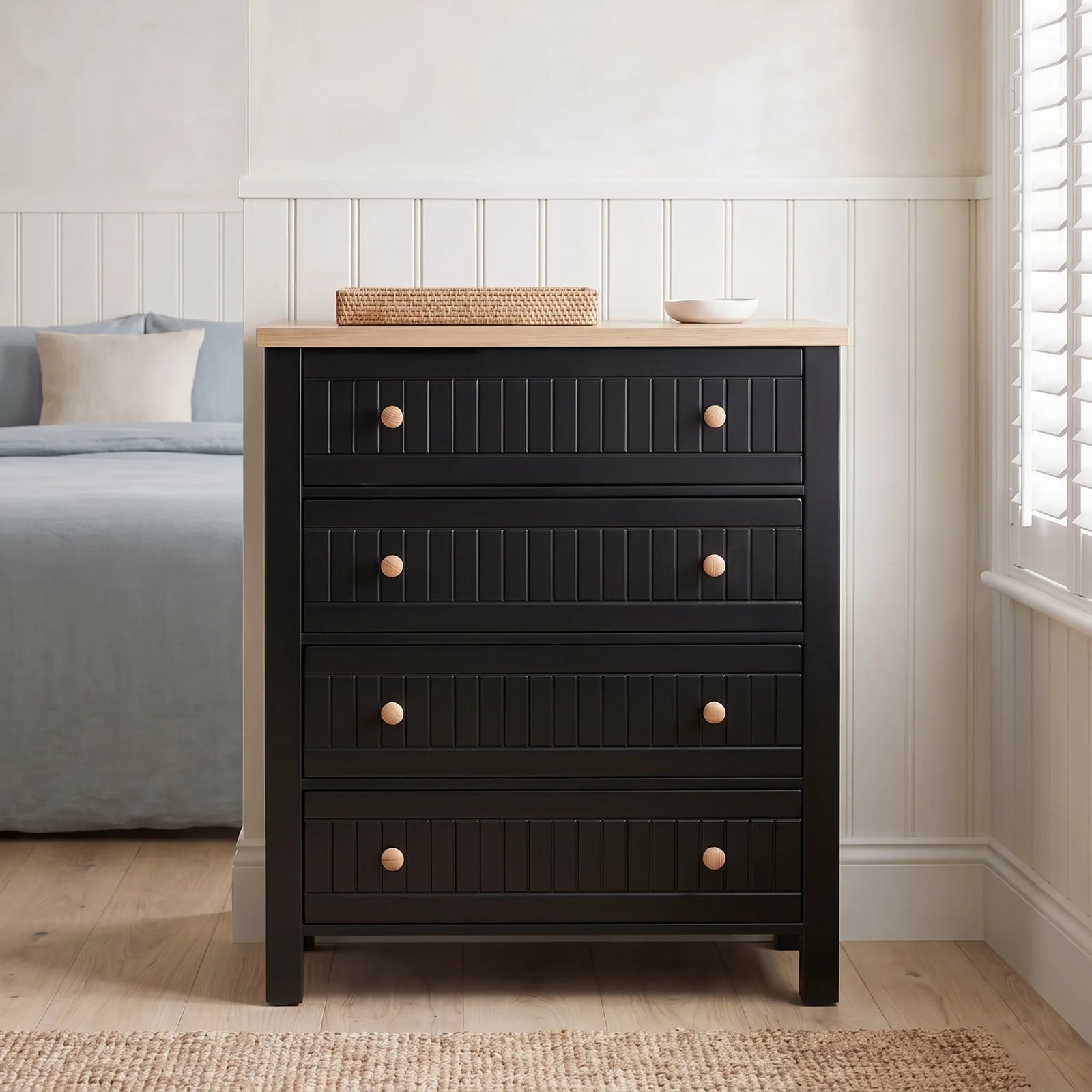 [Black] Linra 4-drawer chest with oak veneer top front view in a modern corner of a attached room with basket and rug