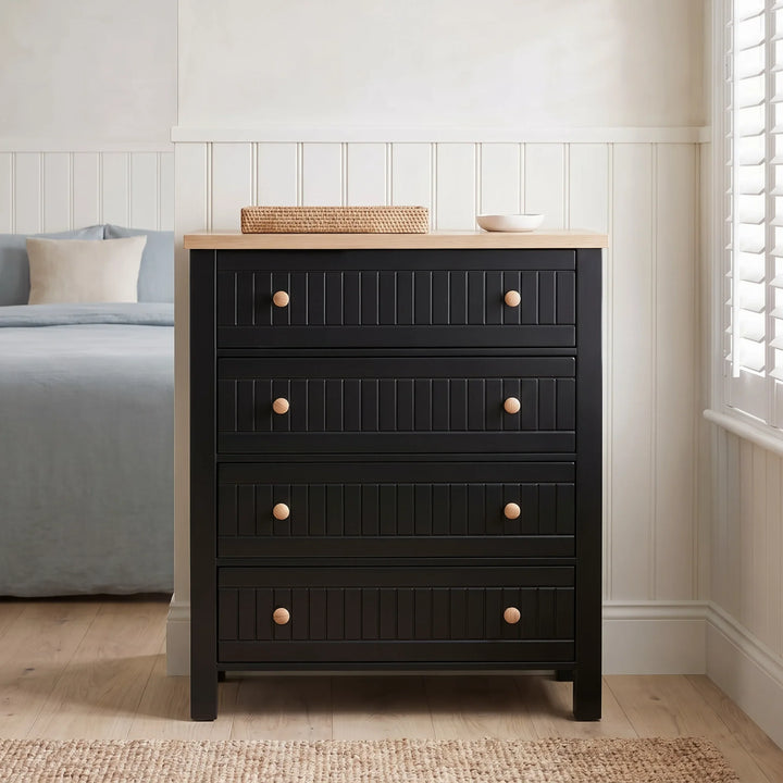 [Black] Linra 4-drawer chest with oak veneer top front view in a modern corner of a attached room with basket and rug