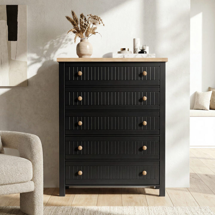 [Black] Linra 5-drawer chest front view in a neutral styled room with dried floral arrangement on oak veneer top