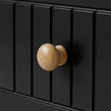 [Black] Close-up of Linra 5-drawer chest oak knob handle against fluted vertical slats on painted black drawer face