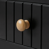 [Black] Close-up of Linra 5-drawer chest oak knob handle against fluted vertical slats on painted black drawer face