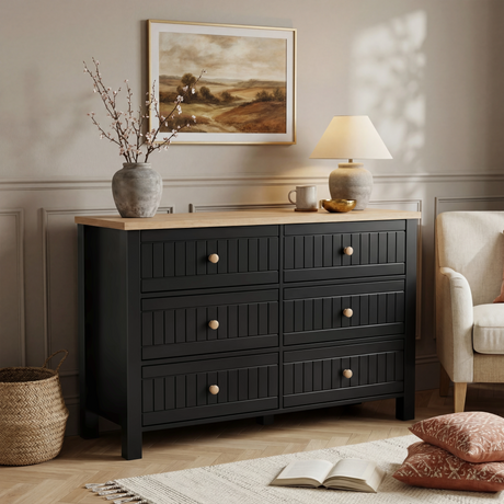 [Black] Linra 6-drawer chest in a bedroom lifestyle setting with armchair, lamp and framed artwork in background