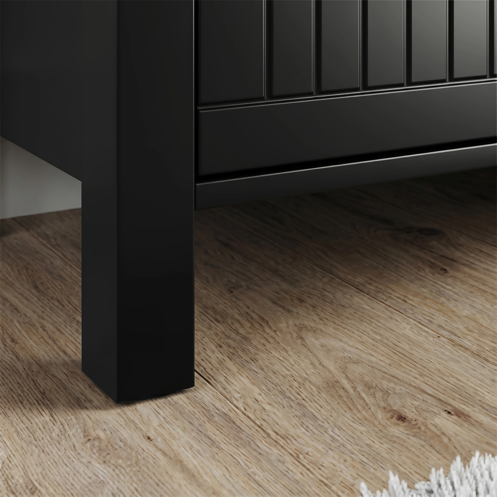 [Black] Detail of Linra 135cm sideboard base, square black leg under beaded door panel on oak-effect flooring