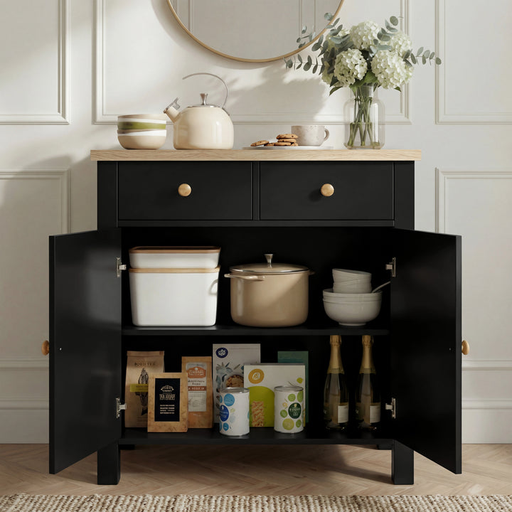 [Black] Linra sideboard interior loaded with kitchenware: kettle, pot, bowls above books and packets on lower shelf