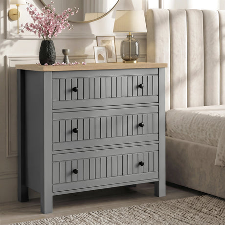 [Grey] Linra 3-drawer chest used as a bedside table in a bedroom with lamp and accessories on oak veneer top