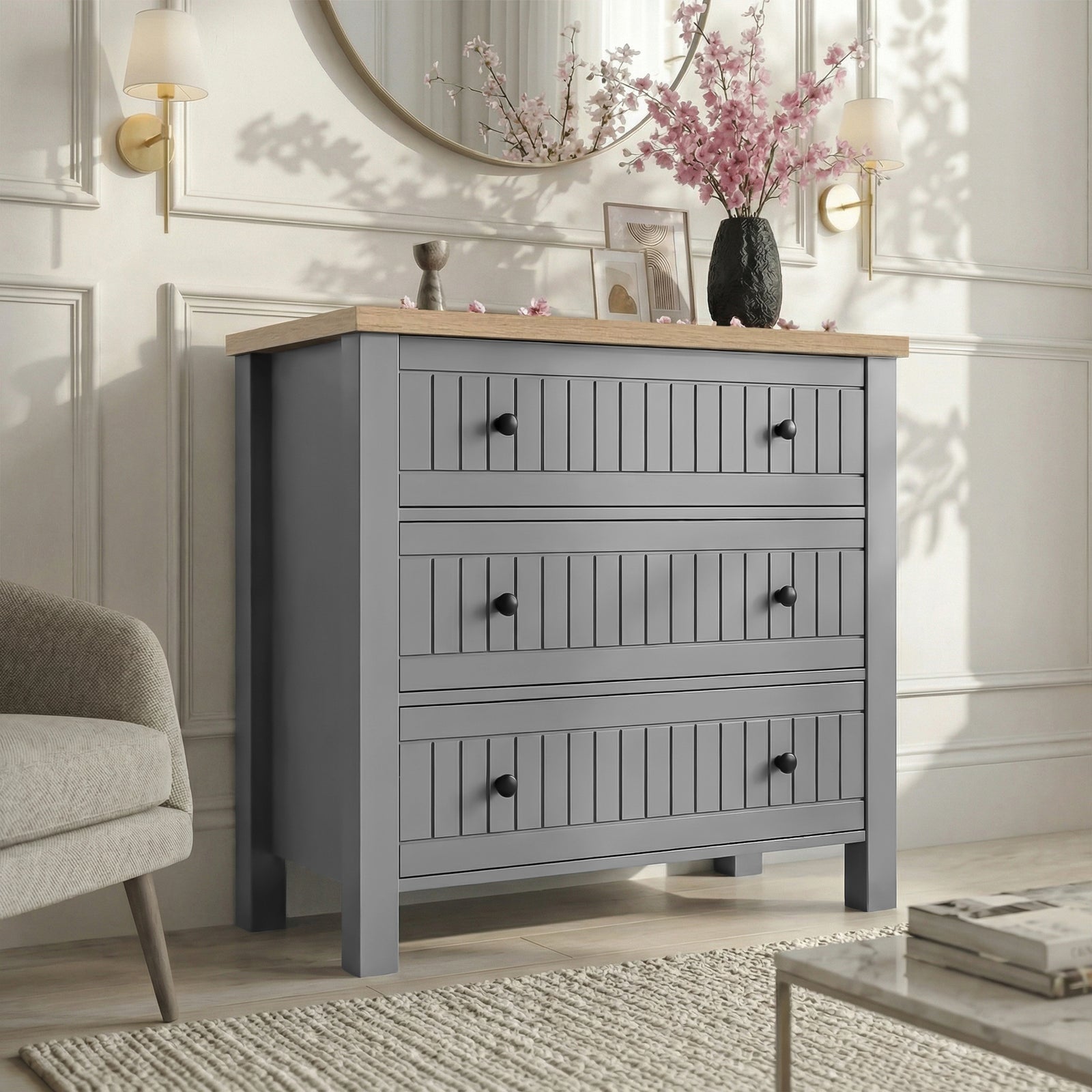 [Grey] Linra 3-drawer chest in a wider bedroom lifestyle setting with armchair and accessories on oak veneer top