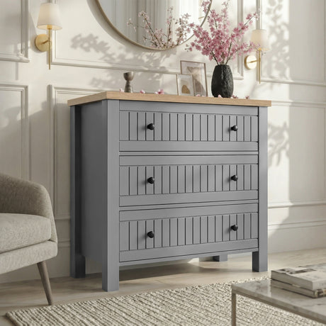 [Grey] Linra 3-drawer chest in a wider bedroom lifestyle setting with armchair and accessories on oak veneer top