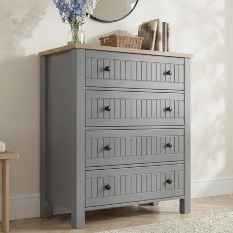 [Grey] Linra 4-drawer chest front view in a styled room with round mirror, books and vase on oak veneer top