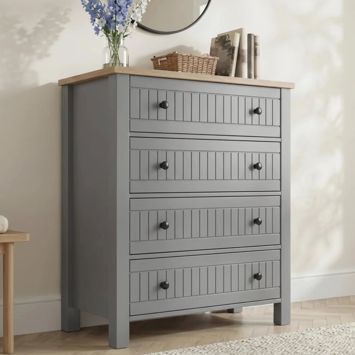 [Grey] Linra 4-drawer chest front view in a styled room with round mirror, books and vase on oak veneer top