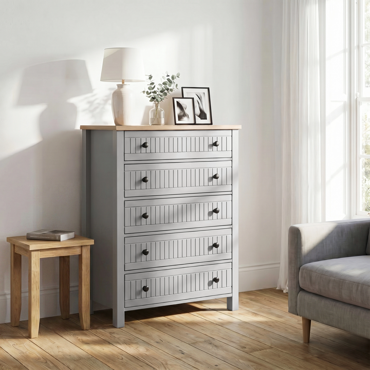 [Grey] Linra 5-drawer chest side lifestyle view in a styled room with armchair and accessories on oak veneer top