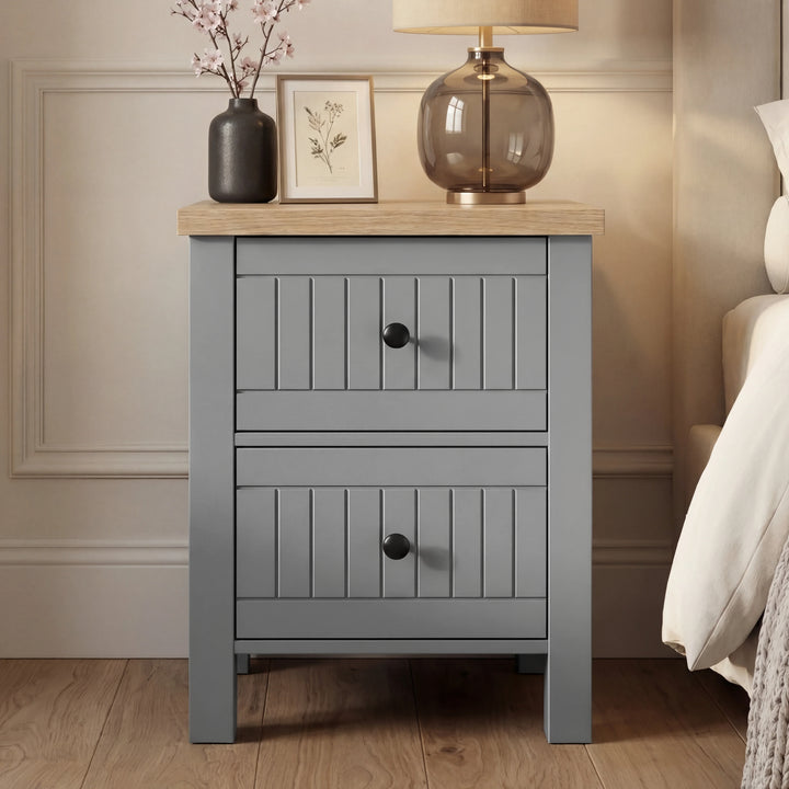[Grey] Linra 2-drawer bedside table front view in a styled bedroom setting with decorative accessories on top