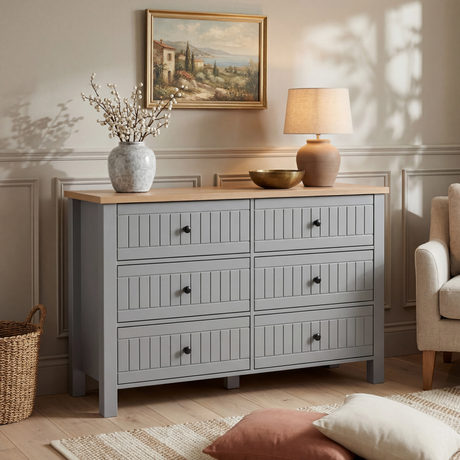 [Grey] Linra 6-drawer chest in a bedroom lifestyle setting with armchair, lamp and framed artwork in background