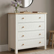 [White] Linra 4 drawer chest angled view with oak top styled with dried floral vase, sculptural ornament, and stacked books below round mirror